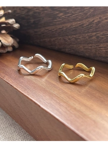 Macro shot of gold and silver wavy open rings on a wooden display with pine cones