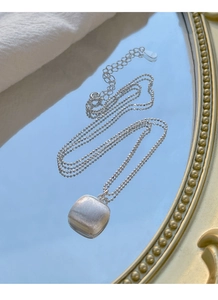 Gros plan détaillé d'un pendentif carré en argent brossé avec une chaîne à billes sur miroir
