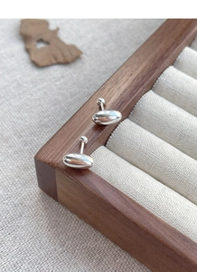 Macro shot of minimalist silver oval stud earrings with high-polish finish on wood