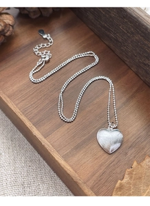 Dettaglio della collana a cuore in argento S925 con finitura spazzolata su base in legno