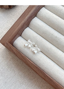 Macro view of S925 silver lily of the valley earrings with bow detail on beige fabric