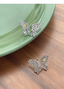 Detail of S925 silver butterfly earrings with engraved wings and tiny yellow floral accents