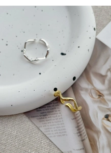 Detailed close-up of gold and silver irregular wavy open rings on a decorative ceramic dish