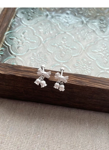Detail of S925 silver lily of the valley earrings with bowknot on dark wood