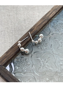 Macro shot of silver C-shaped bead earrings on vintage glass and wood display