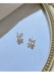 Detailed macro view of S925 silver lily of the valley bow earrings on a mirror surface