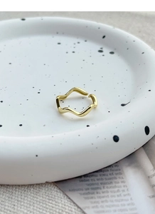 Detail of adjustable gold wave ring with minimalist irregular curved design on ceramic