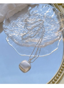 Détail du pendentif carré en argent brossé avec chaîne à billes sur plateau bleu