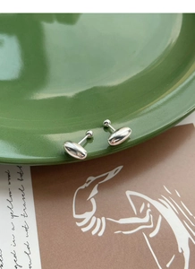 Macro view of minimalist oval silver studs on a ceramic plate with a vintage card background