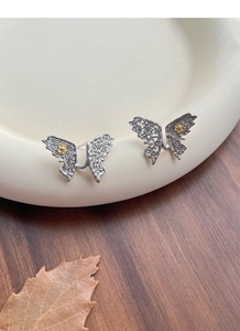 Detailed macro view of S925 silver butterfly earrings with golden flower accents on ceramic