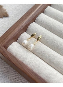Détail de clous d'oreilles en goutte dorée avec perles baroques sur présentoir en bois