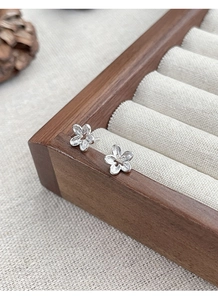 Close-up of minimalist S925 sterling silver hollow flower stud earrings on wooden box