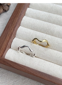 Close-up of minimalist wave-shaped gold and silver rings in a luxury wooden jewelry box