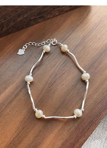 Macro detail of S925 silver wavy tube bracelet with freshwater pearls and heart charm
