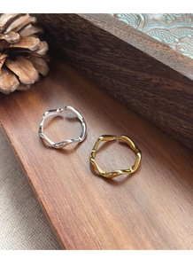 Detail of silver and gold wave-shaped open rings on vintage wooden table with pine cones