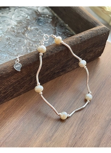 Macro detail of S925 sterling silver curved bar bracelet with freshwater pearls and heart charm