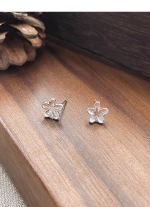 Detail of S925 sterling silver hollow flower stud earrings on a rustic wooden background