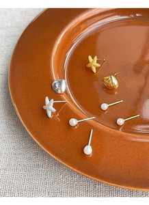 Dettaglio macro di orecchini a stella marina e conchiglia con perle su piatto decorato
