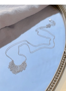 Detail of S925 silver fringe heart necklace on a mirror reflecting a clear blue sky