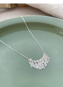 Detail shot of silver fringe pendant necklace on a minimalist green ceramic plate