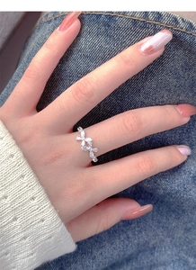Detail of silver bow ring with marquise zircons worn on hand against denim background