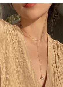 Collier en Y doré avec une perle ronde porté sur une tenue élégante à plis fins