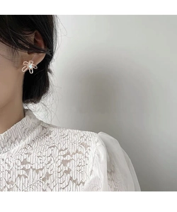 Dettaglio orecchino a fiore dorato con perla su modella con pizzo bianco fine