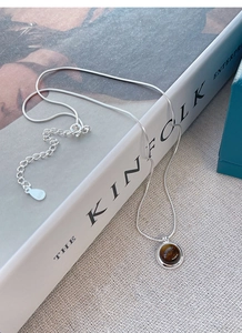 Detail of S925 silver necklace with round tiger eye pendant on a textured fabric surface