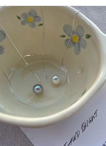 Detailed view of silver-tone snake chains with grey and white round pearls in a ceramic bowl
