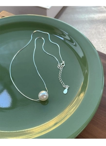 Detailed close-up of S925 silver necklace with round white pearl on dark green ceramic plate