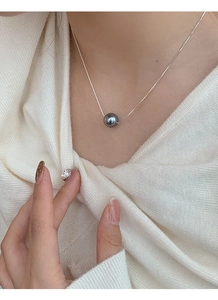 Close-up of deep grey pearl pendant on silver snake chain worn on a white cardigan