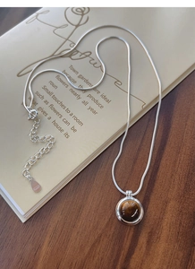 Detailed macro of tiger eye stone pendant with adjustable silver chain on vintage books