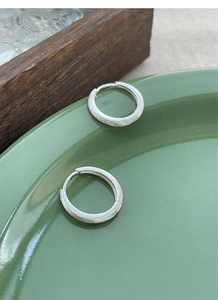 Macro detail of brushed matte S925 sterling silver hoop earrings on ceramic plate