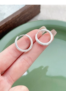Detail of matte brushed S925 sterling silver hoop earrings held by hand for size reference