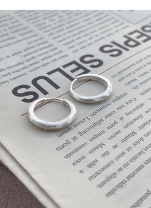 Macro shot of minimalist silver hoop earrings with a textured brushed matte finish
