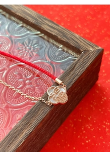 Vue macro d'un charm trèfle avec nacre blanche et symbole Fu sur un bracelet rouge tressé