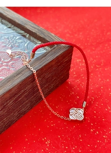 Détail macro du pendentif Fu en argent S925 sur bracelet tressé rouge et chaîne rose
