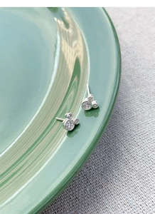 Détail de boucles d'oreilles souris en argent avec zircons sur un plateau vert