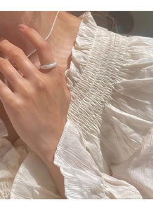 Close-up of a sparkling frosted silver ring worn with a delicate necklace and white lace top