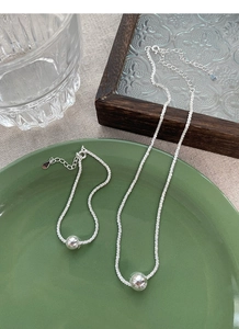 Detail view of silver bead necklace and bracelet set on a green ceramic plate