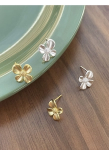 Detailed close-up of matte silver and gold gardenia earrings on a ceramic dish