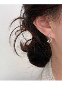 Close-up of silver star and moon earrings with clear zircon stone on model's ear