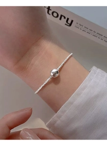 Detail of a minimalist silver snake chain bracelet with a polished round metal bead