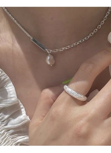 Detailed close-up of frosted silver ring and rectangular pendant necklace with pearl