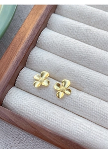 Detailed close-up of matte gold gardenia flower studs on a cream fabric ring slot