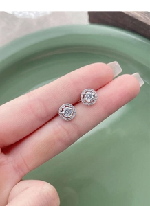 Gros plan de boucles d'oreilles halo en argent S925 avec zircons tenues à la main