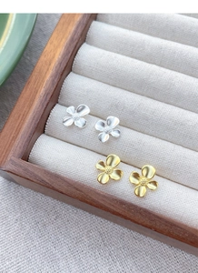 Detailed view of silver and gold matte gardenia stud earrings on a velvet display tray