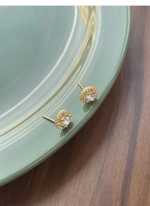 Détail de boucles d'oreilles halo dorées avec zircone cubique sur un plat en céramique