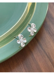 Macro shot of matte silver gardenia flower earrings on a dark green ceramic plate
