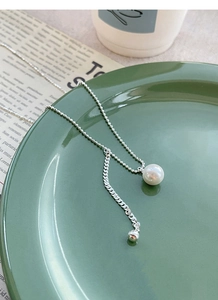 Detail of silver S925 Y-shaped pearl necklace with curb chain tassel on green plate